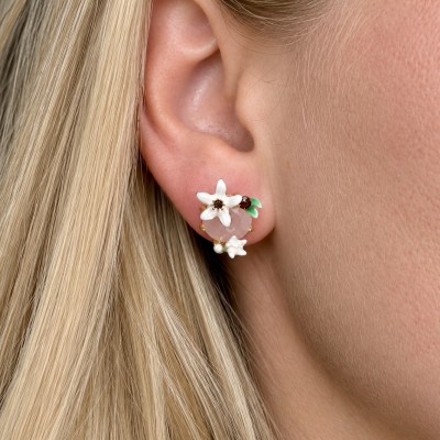 Pendientes florales blancos con piedra rosa y detalles esmaltados en oreja de mujer