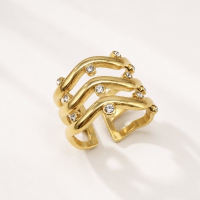 Anillo ajustable dorado con circonitas y diseño ondulado de acero inoxidable sobre fondo beige elegante