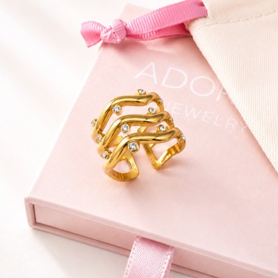 Anillo ondulado dorado con circonitas sobre caja rosa AdoraVi joyería elegante y minimalista