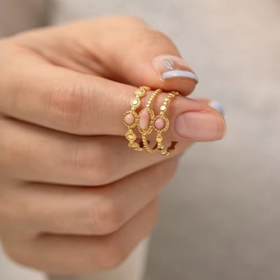 Anillo triple de cuarzo rosa colocado en una mano con manicura natural.