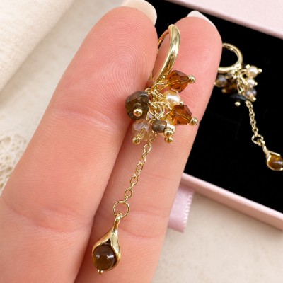 Detalle de pendientes largos dorados con cristales color ámbar y perla