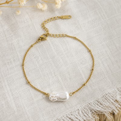 Pulsera minimalista con perla barroca natural sobre fondo de lino en color beige.
