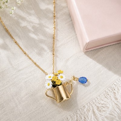 Collar con regadera y flores esmaltadas sobre tela beige y caja rosa AdoraVi.