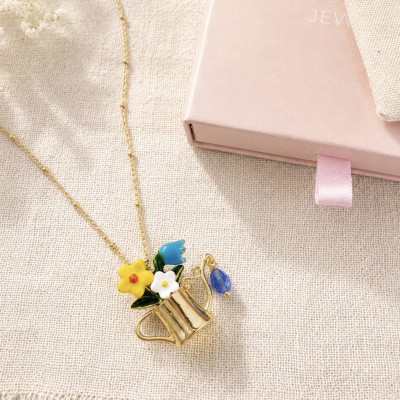 Collar regadera con flores esmaltadas azules y amarillas sobre tela de lino beige y caja rosa AdoraVi.
