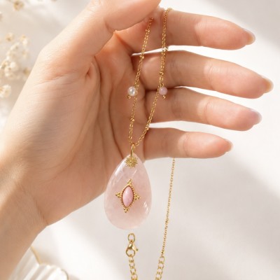 Primer plano del colgante de cuarzo rosa natural con detalles dorados sostenido en la mano