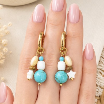 Pendientes artesanales con piedras naturales turquesa y nácar sobre mano.