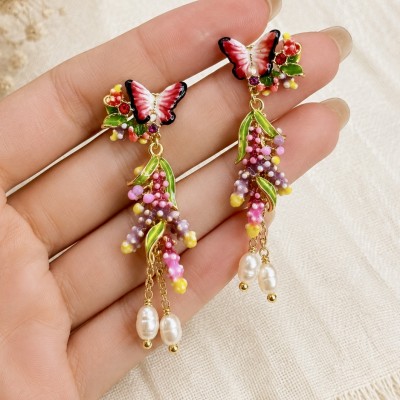 Pendientes largos florales con mariposa y perlas sujetados en mano femenina detalle artesanal